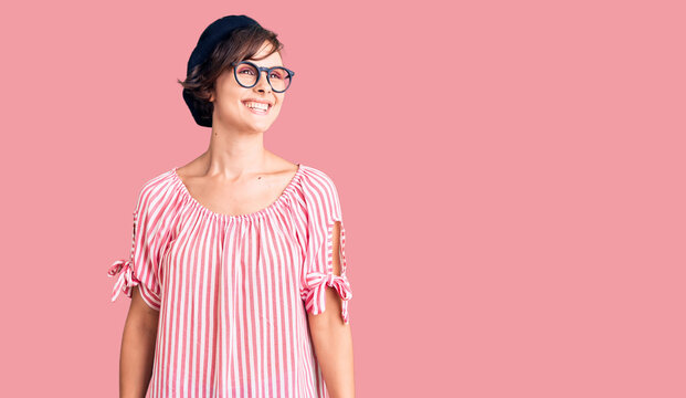 Beautiful young woman with short hair wearing casual clothes and glasses looking away to side with smile on face, natural expression. laughing confident.
