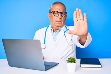 Senior handsome man with gray hair wearing doctor uniform working using computer laptop doing stop sing with palm of the hand. warning expression with negative and serious gesture on the face.