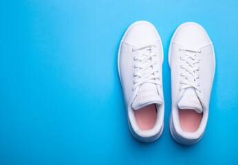 Pair of stylish sport shoes on blue background. Top view of white sneakers on color background with place for text