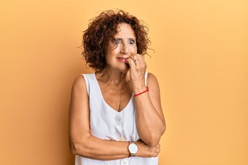 Beautiful middle age mature woman wearing casual clothes looking stressed and nervous with hands on mouth biting nails. anxiety problem.