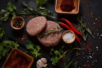 Raw beef hamburger patties with herbs and spices. Raw burger cutlets on a concrete background