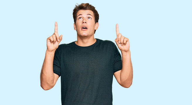 Handsome caucasian man wearing casual clothes amazed and surprised looking up and pointing with fingers and raised arms.