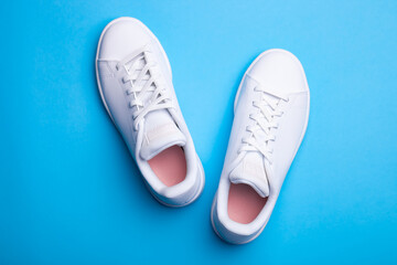 Pair of stylish sport shoes on blue background. Top view of white sneakers on color background
