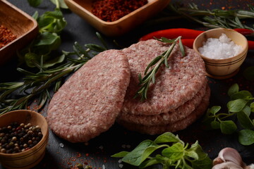 Raw beef hamburger patties with herbs and spices. Raw burger cutlets on a concrete background
