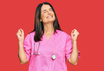 Middle age brunette woman wearing doctor uniform and stethoscope very happy and excited doing winner gesture with arms raised, smiling and screaming for success. celebration concept.