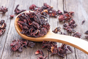 Dried hibiscus flower in wooden spoon or bowl on wooden table, alternative medicine