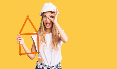 Beautiful caucasian woman with blonde hair wearing architect hardhat and holding tools smiling...