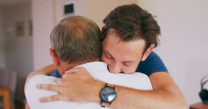 A smiling young man hugs his elderly father at home.
