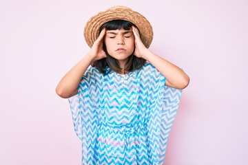 Young little girl with bang wearing summer dress and hat suffering from headache desperate and stressed because pain and migraine. hands on head.