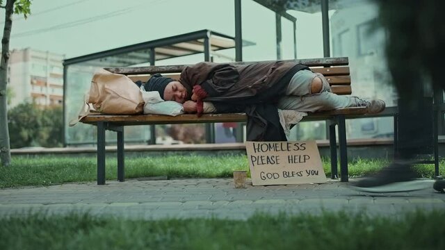 Homeless person sleeping on a park bench, indifferent people walking by