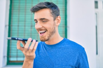 Young caucasian man smiling happy sending voice message using smartphone at the city.