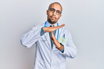 Hispanic adult man wearing doctor uniform and stethoscope doing time out gesture with hands,...