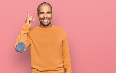 Hispanic adult man wearing casual winter sweater pointing finger up with successful idea. exited and happy. number one.
