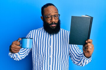 Young african american man reading book and drinking a cup of coffee skeptic and nervous, frowning...