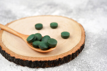 Obraz na płótnie Canvas Spirulina tablets in wooden spoon on round stand, light concrete background. Nutrition, vitamin, immunity concept. Close-up, copy space