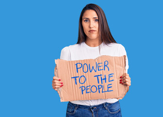 Young beautiful woman holding power to the people cardboard banner thinking attitude and sober expression looking self confident