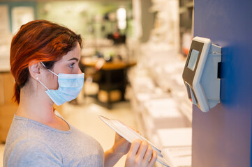 A woman in a medical mask scans the price of an item in a store. An electronic price checker on the...