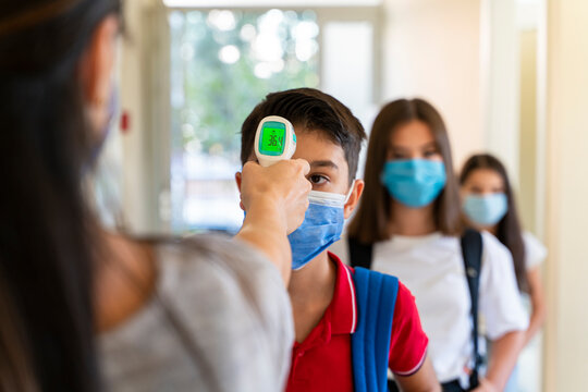 Teacher checking temperature of students with face mask for pandemic while children go back to school