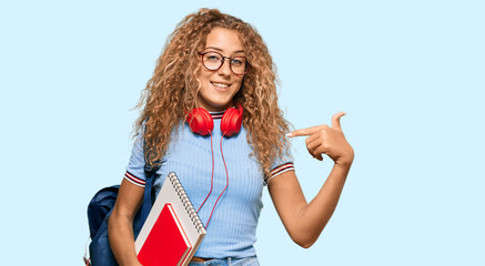 Beautiful caucasian teenager girl holding student backpack and books pointing finger to one self...