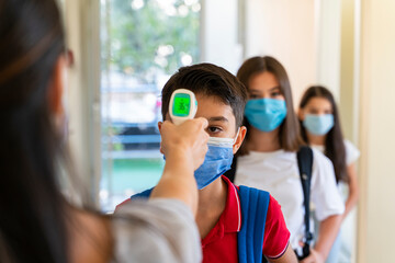 Teacher checking temperature of students with face mask for pandemic while children go back to school