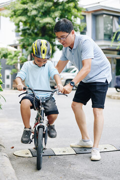 Father helping preteen son who is riding bicycle for the first time