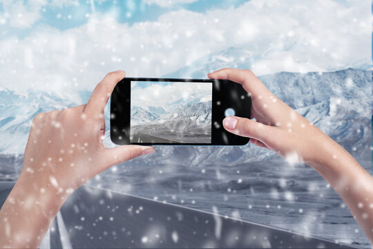 A woman takes photos of a snowy landscape with her smartphone. Close-up of women's hands. Cell phone. Telephone. Mobility and modern lifestyle concept. snowy winter road in the mountains.