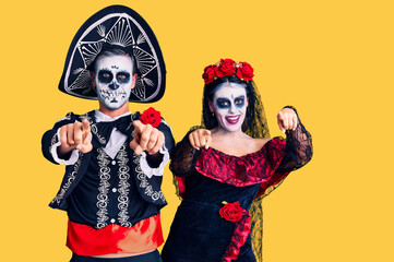 Young couple wearing mexican day of the dead costume over background pointing to you and the camera with fingers, smiling positive and cheerful