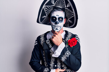 Young man wearing mexican day of the dead costume over white with hand on chin thinking about question, pensive expression. smiling with thoughtful face. doubt concept.