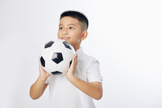 Smiling Vietnamese preteen boy ready to throw soccer ball, isolated on white