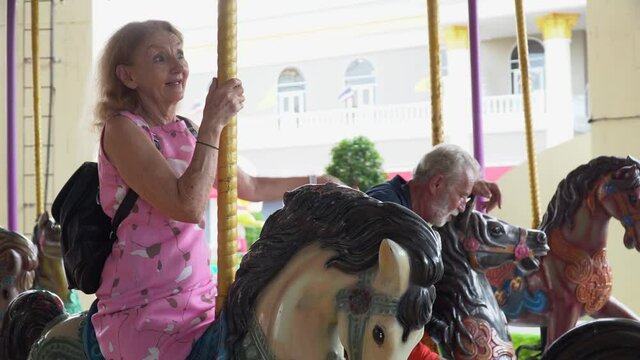 Happy senior couple riding on carousel together  at the amusement park outdoors in summer . crazy old man and funny mature woman  having fun in vacation