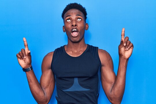 Young african american man wearing sportswear amazed and surprised looking up and pointing with fingers and raised arms.