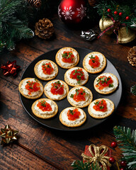 Salmon caviar and soft cheese savory crackers with decoration, gifts, green tree branch on wooden rustic table.