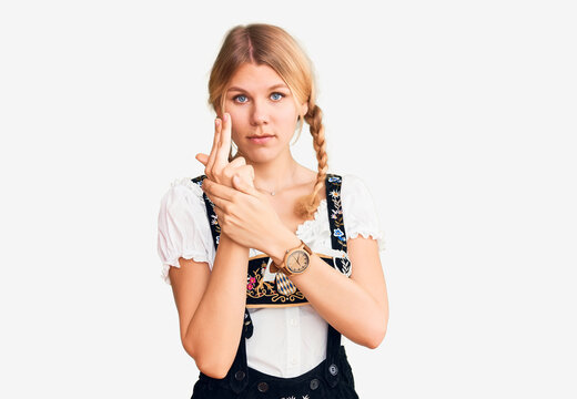 Young beautiful blonde woman wearing oktoberfest dress holding symbolic gun with hand gesture, playing killing shooting weapons, angry face