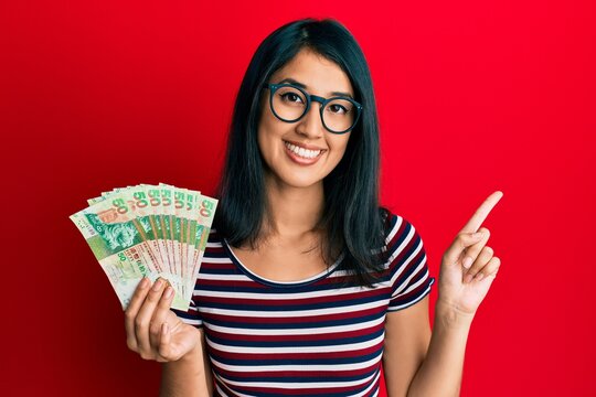 Beautiful asian young woman holding 50 hong kong dollars banknotes smiling happy pointing with hand and finger to the side