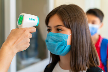 Teacher checking temperature of students with face mask for pandemic while children go back to school