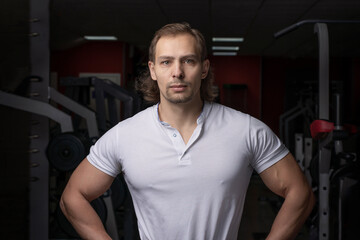 Fototapeta na wymiar Personal trainer, portrait of a male athlete in a white shirt on the background of the gym