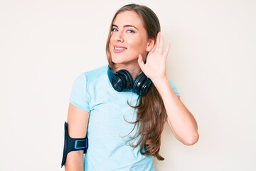 Obraz premium Beautiful young caucasian woman wearing gym clothes and using headphones smiling with hand over ear listening an hearing to rumor or gossip. deafness concept.