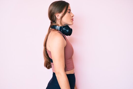Beautiful young caucasian woman wearing gym clothes and using headphones looking to side, relax profile pose with natural face with confident smile.