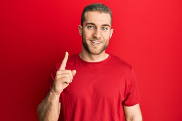 Fototapeta premium Young caucasian man wearing casual clothes smiling with an idea or question pointing finger up with happy face, number one