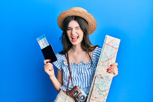 Young beautiful caucasian girl holding passport and city map winking looking at the camera with sexy expression, cheerful and happy face.