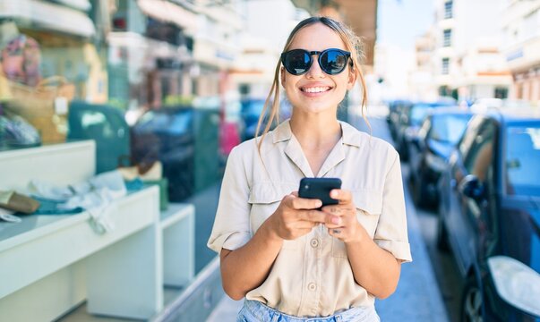 Young beautiful blonde caucasian woman smiling happy outdoors on a sunny day using smartphone