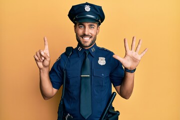 Handsome hispanic man wearing police uniform showing and pointing up with fingers number six while smiling confident and happy.