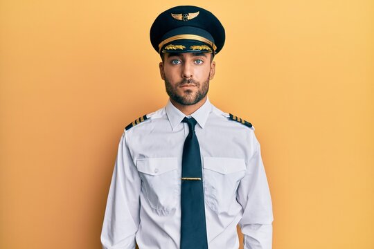 Handsome hispanic man wearing airplane pilot uniform relaxed with serious expression on face. simple and natural looking at the camera.