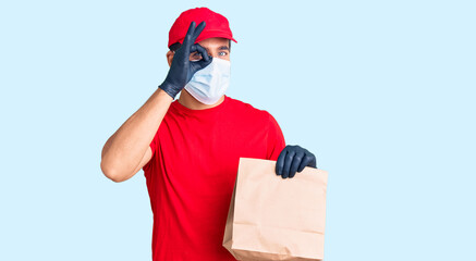 Young hispanic man delivering food wearing covid-19 safety mask holding paper bag smiling happy doing ok sign with hand on eye looking through fingers
