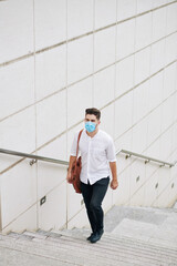 Handsome young man in medical mask walking up the stairs