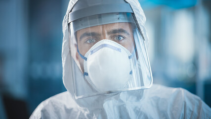 Dramatic Shot of Heroic and Overworked Medical Worker Wearing Coverall, Face Mask and Shield Looks...