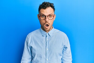 Young hispanic man wearing casual clothes and glasses afraid and shocked with surprise and amazed expression, fear and excited face.