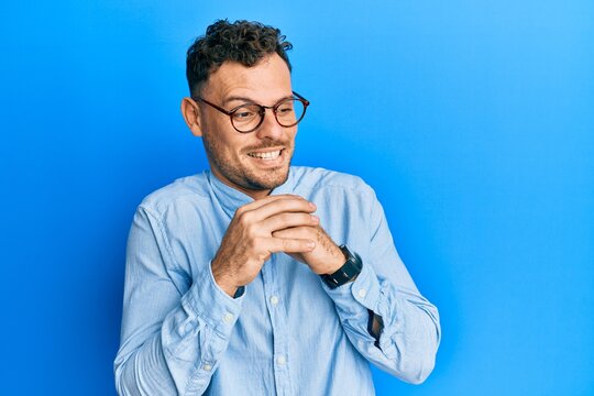 Young hispanic man wearing casual clothes and glasses laughing nervous and excited with hands on chin looking to the side