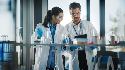 Medical Science Laboratory with Diverse Team of Research Scientists Working. Microbiologist Working with Biochemists using Micropipette Dropper and Digital Tablet Computer.