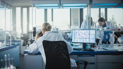Medical Laboratory with Team of Scientists Working. Microbiologist Looking under Microscope and...